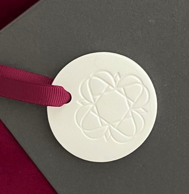 
                  
                    Anara Emblem Keepsake with burgundy ribbon on a grey box
                  
                