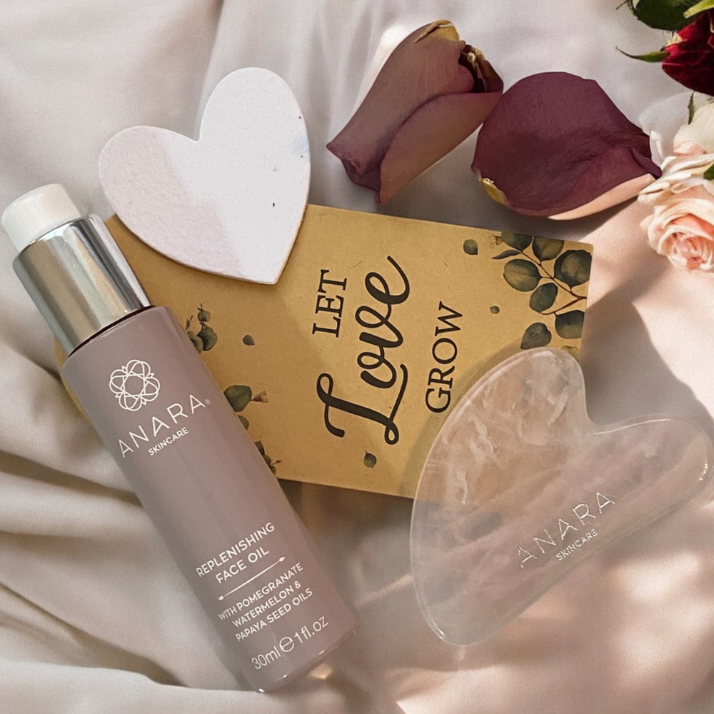 Anara Skincare Replenishing Face Oil, Rose Quartz Gua Sha and heart seed paper with a let love grow envelope and rose petals on a cream fabric